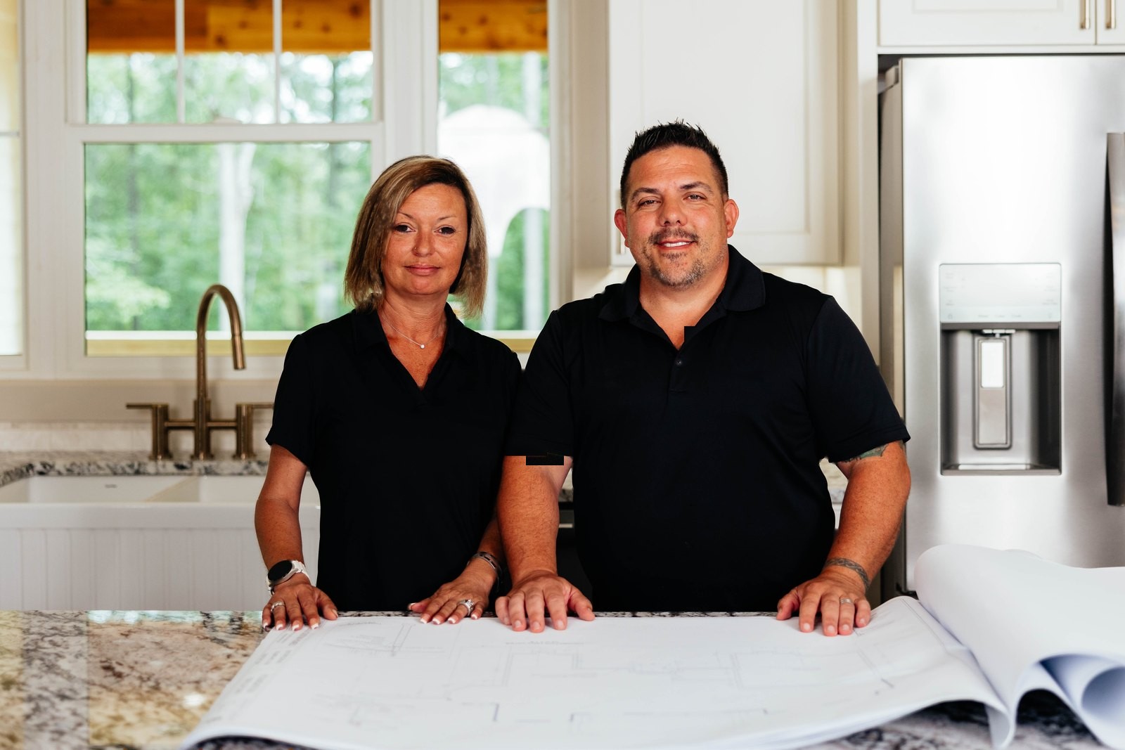 Jason and Jessica, the founders of Level Ground, standing over a set of house plans